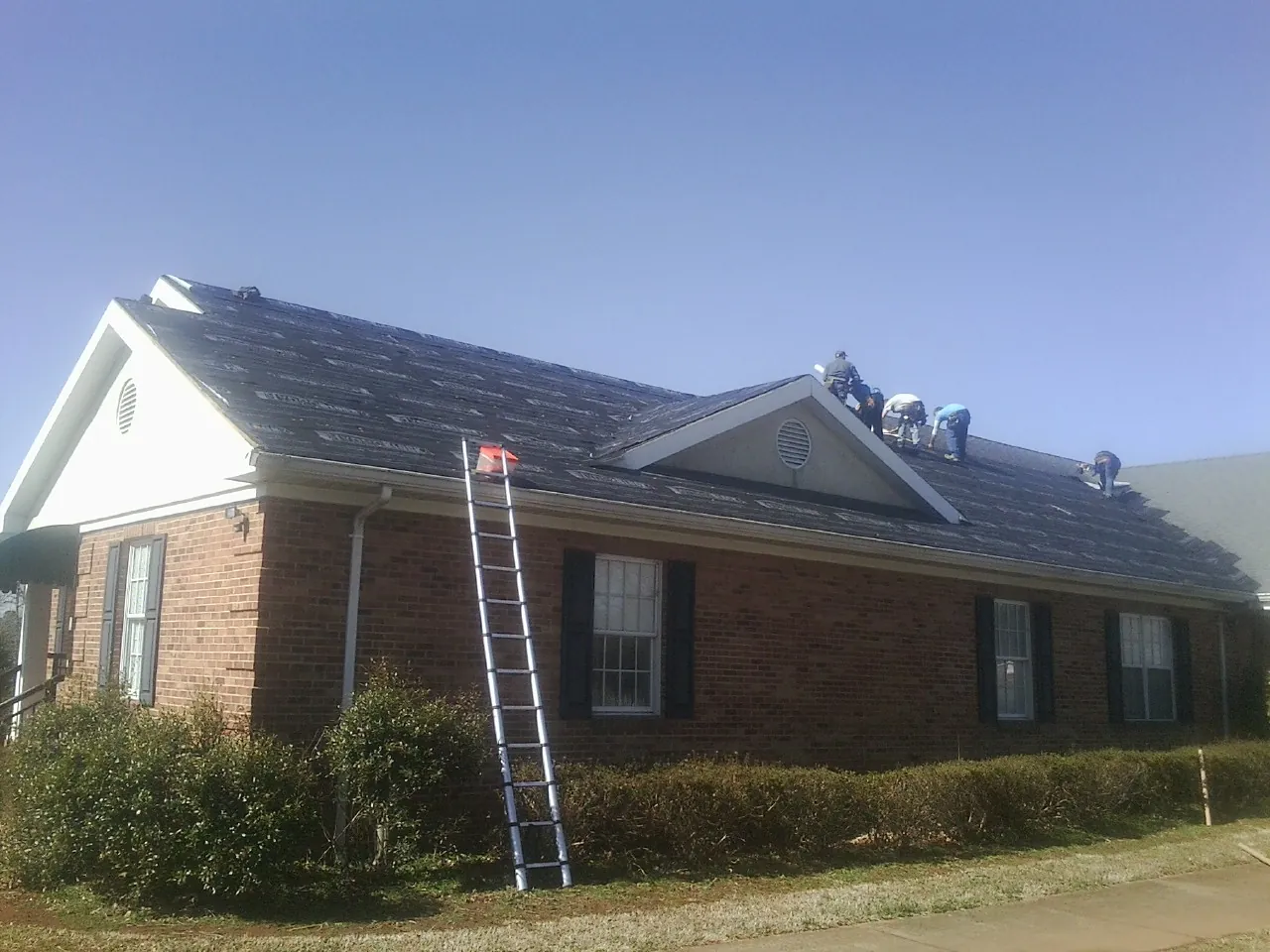 Crew tearing shingles off a brick ranch roof with a ladder set — Metal Roof Repair work by our crew in Lenox