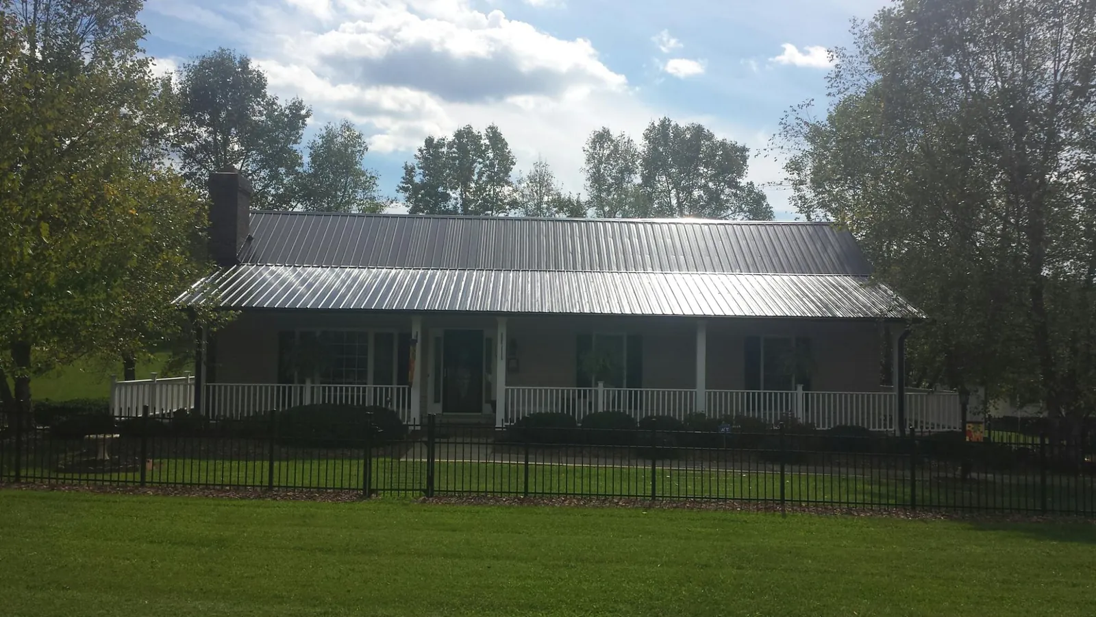 Gray metal roof on a brick ranch with a full width front porch — Gutter Guard Installation work by our crew in Lenox